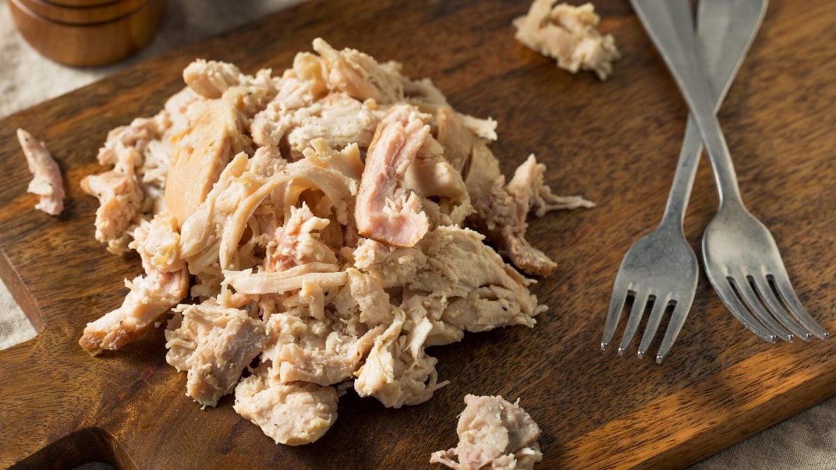 Eine Portion Pulled Chicken liegt auf einem braunen Holzbrett. Neben dem Pulled Chicken liegen zwei silberne Gabeln.