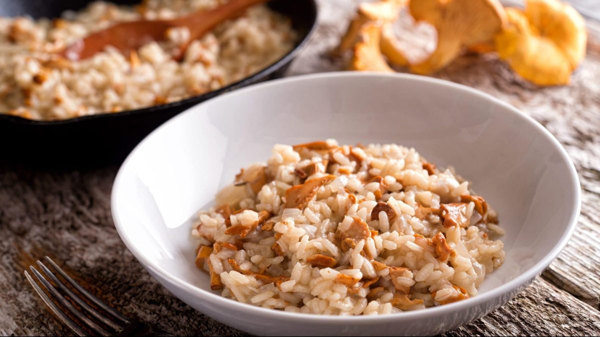 Auf einem rustikalem Tisch steht ein runder Teller, in dem ein Pfifferling-Risotto ist.