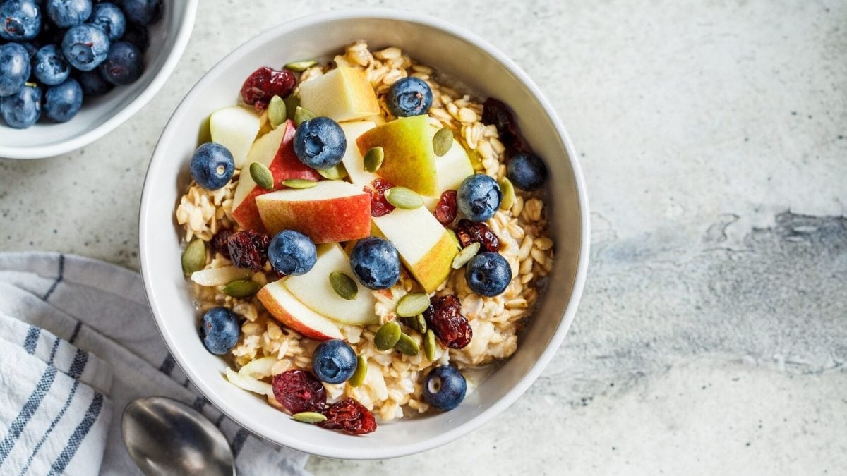 Apfelschnitze, Blaubeeren, getrocknete Cranberries, Pistazien, Walnüsse und Haferflocken toppen den Joghurt in einer Schüssel und ergeben das Bircher Müsli.