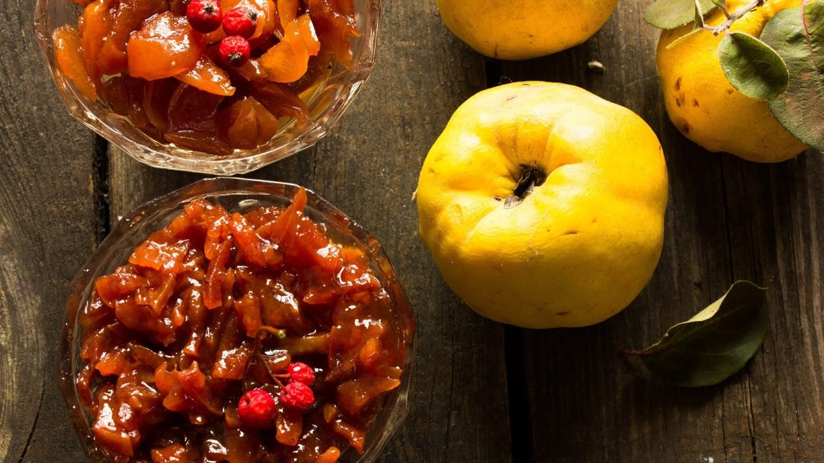Chutney mit Quitten und Äpfeln in zwei Glasschüsseln angerichtet neben frischen Quitten vor einem Holz-Hintergrund von oben.
