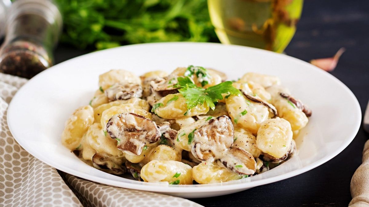 Auf dem Bild ist ein weißer Teller mit Gnocchi in Pilz-Käse-Sauce .