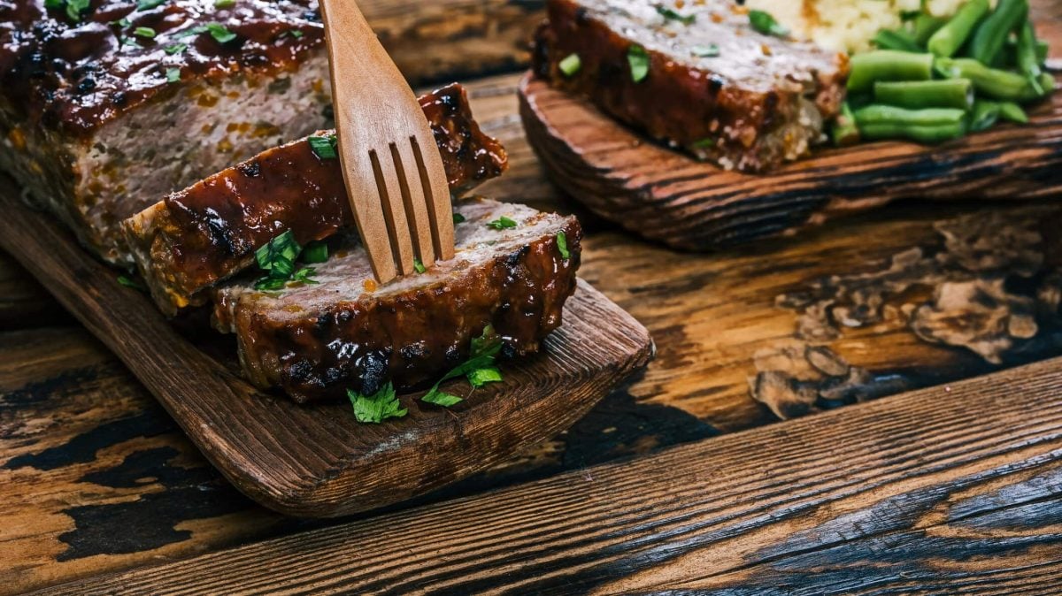Auf zwei Holzbrettern liegen einige Scheiben Hackbraten mit Spinat und Feta, daneben grüne Bohnen.