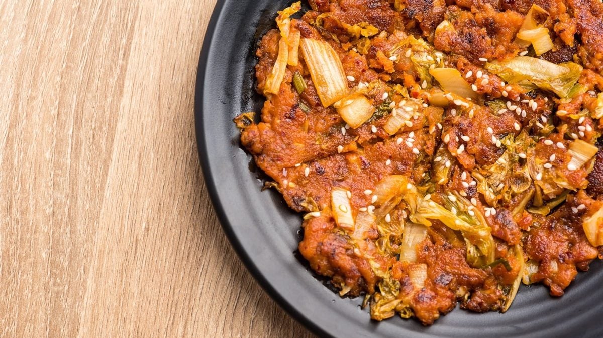 Ein Kimchi Jeon, ein koreanischer Pfannkuchen mit Kimchi, auf einem schwarzen Teller vor einem Holzhintergrund, von oben.