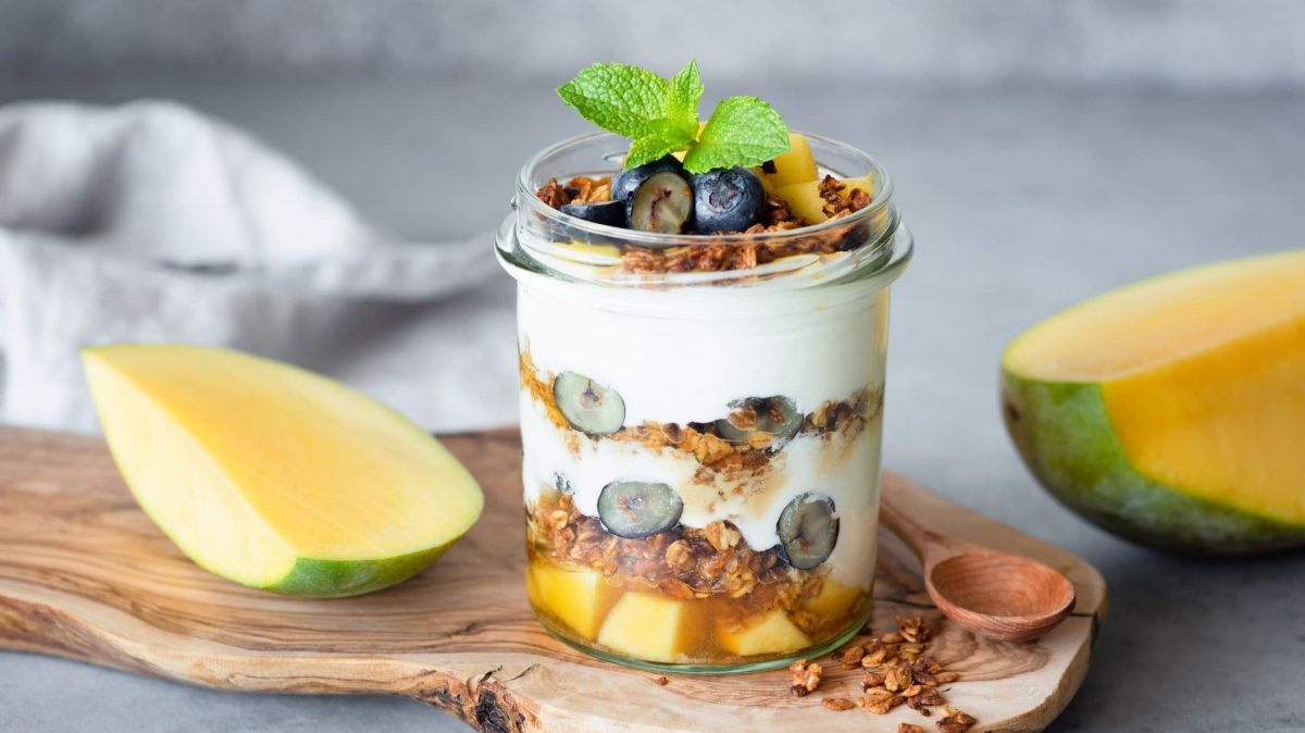 Knuspriges Granola mit Nüssen, Beeren und Mango in einem Glas.