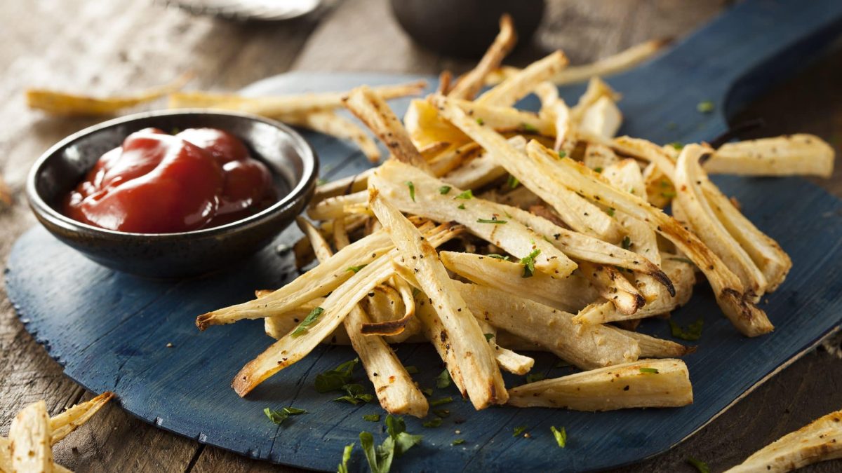 auf einem dunklen Holzbrett liegen Pommes aus Petersilienwurzeln. Danebenn stehte eine kleine Schale mit Ketchup