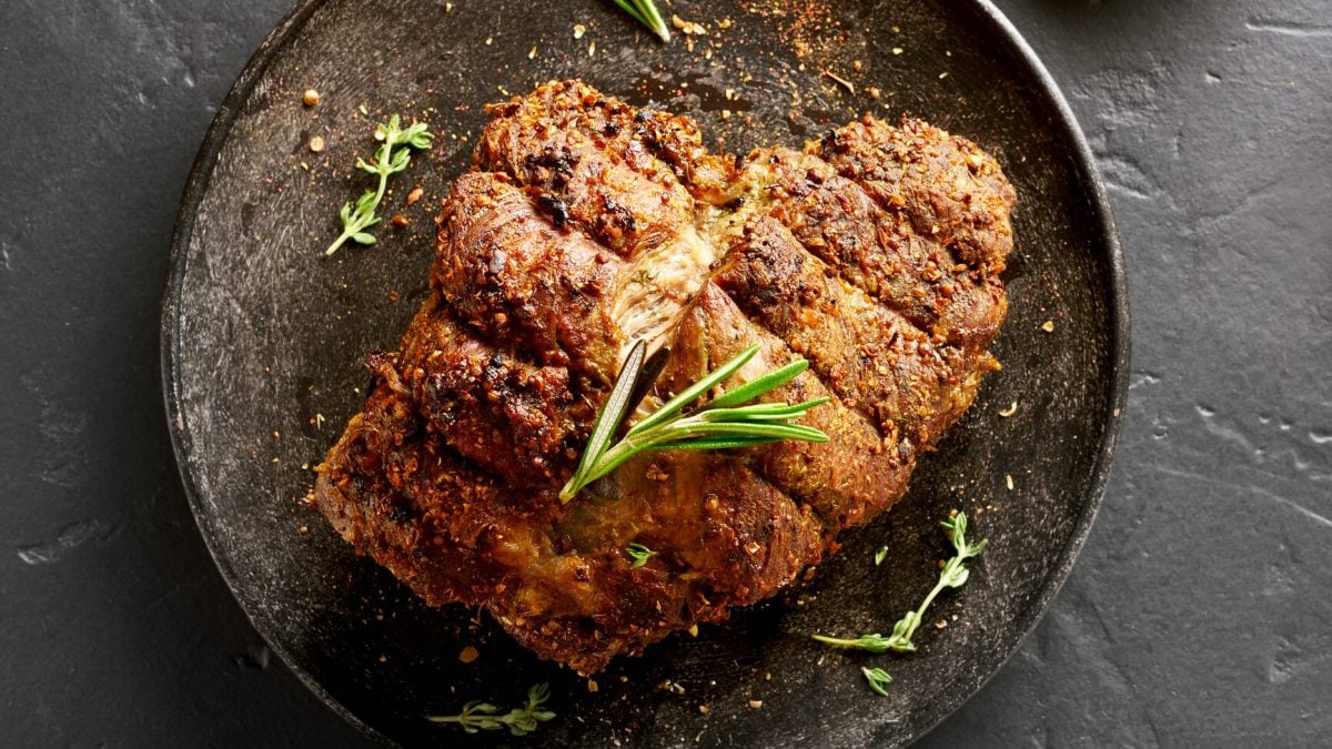 Ein dunkler Teller in der Draufsicht mit Schweinekrustenbraten, der mit Apfel-Portweinsoße serviert wird.