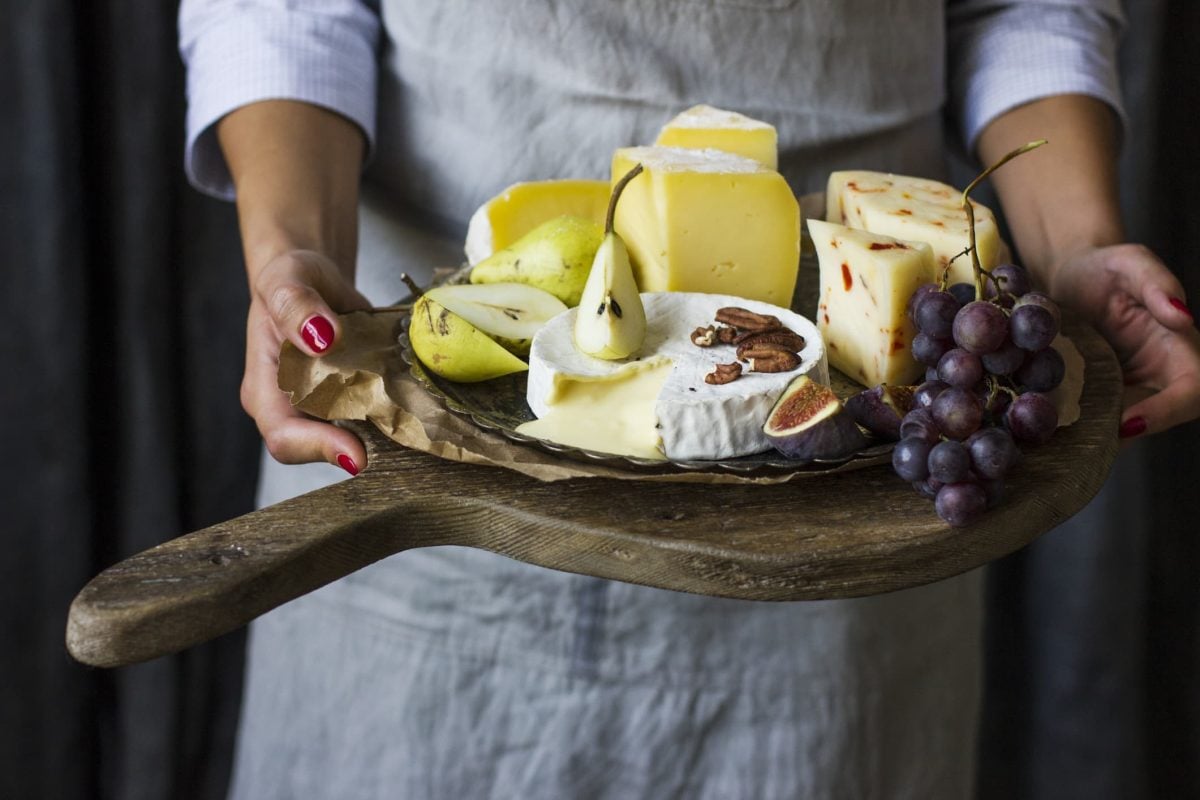 Was ist Lab? Eine Frau hält ein großes Holzbrett mit vielen verschiedenen Käse- und Obstsorten in den Händen.