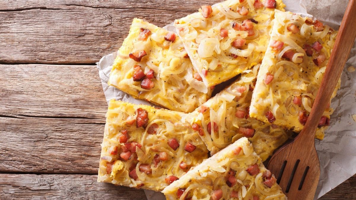 Auf Holzbrettern liegen fünf Stück Zwiebelkuchen mit Speck.