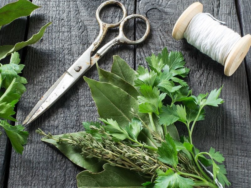Auf einem Tisch liegt ein gebundenes Sträußchen mit Kräutern. Es handelt sich um ein Bouquet garni.