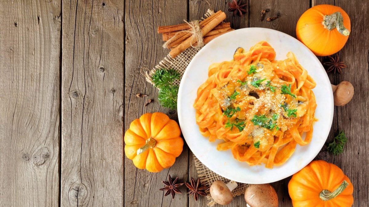 Unsere Butternut-Pasta mit Champignons auf einem weißen Teller. Die Pasta ist angerichtet mit Parmesan und Petersilie. Der Teller steht auf einem braunen Untergrund.