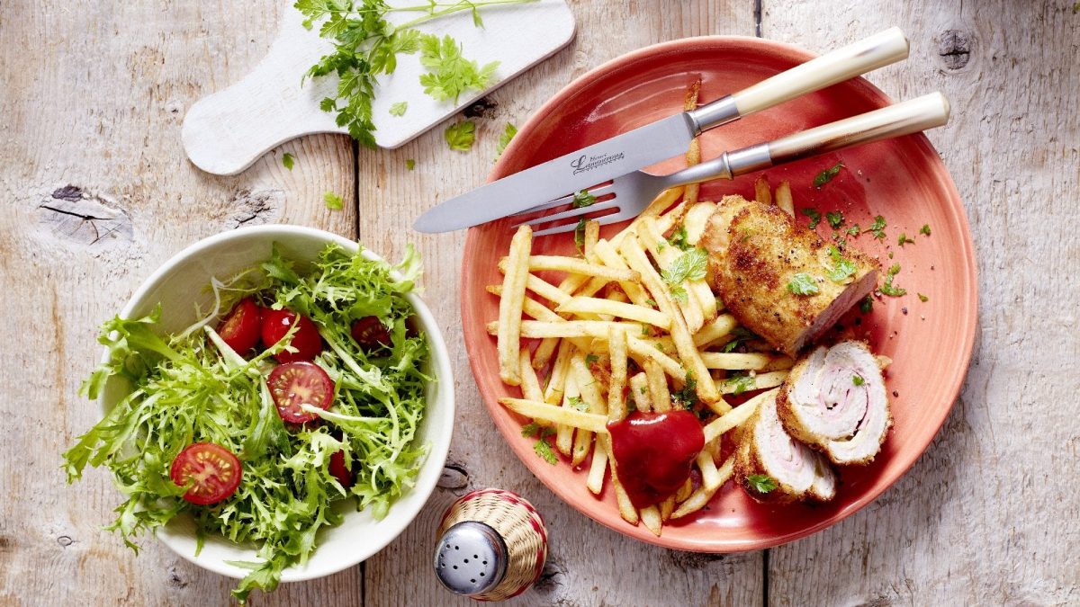 Die angeschnittene Cordon bleu-Roulade serviert auf einem Teller. Dazu gibt es einen grünen Salat mit Tomaten.