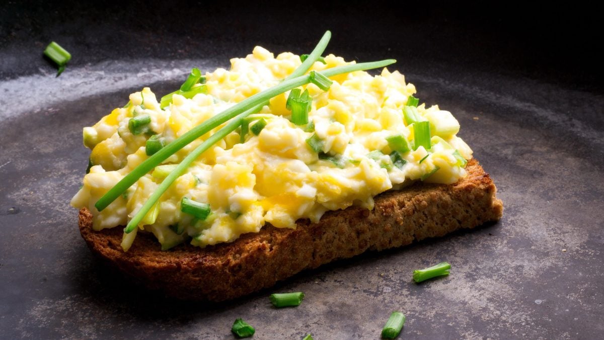 Brot belegt mit Eiersalat und Schnittlauch auf dunkler Arbeitsfläche.