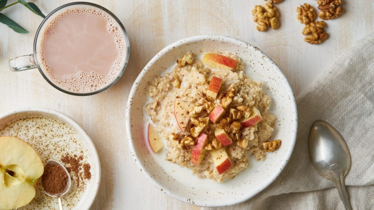 Der Haferbrei mit Nüssen und Apfel ist in einer weißen Müslischale angerichtet. Dazu gibt es eine Tasse Kakao.