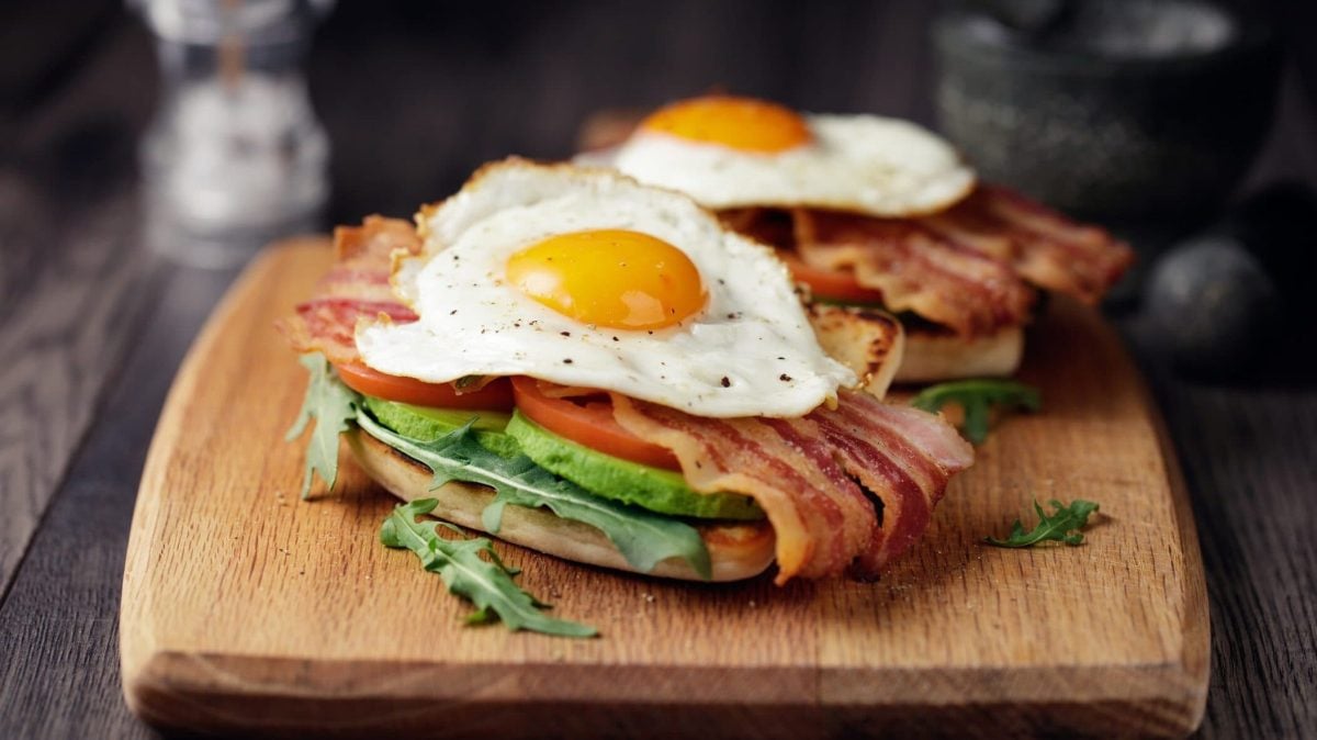 Die Avocado-Ei-Bacon-Stulle rustikal angerichtet auf einem Holzbrett.