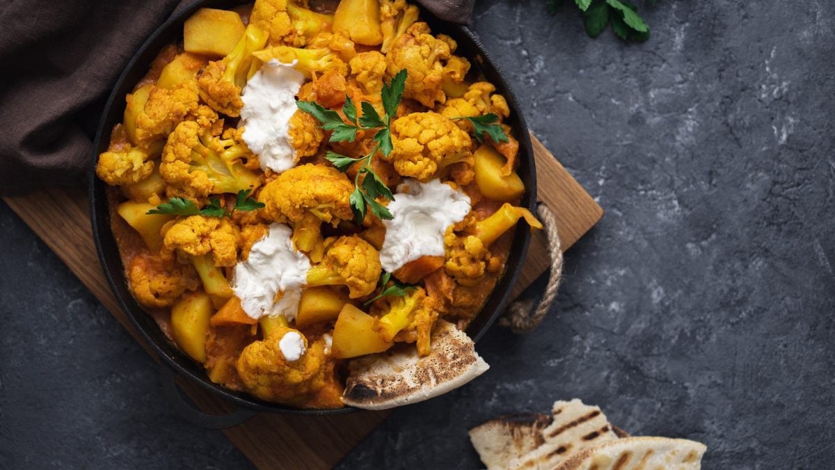 EIn Topf mit Blumenkohl-Curry und Joghurt, daneben liegt etwas Naanbrot.