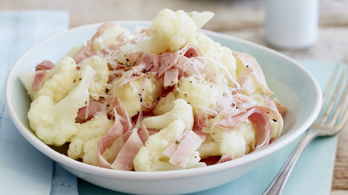 Feinste Blumenkohlröschen mit Schinkenstreifen und Parmesan in einem Teller angerichtet.