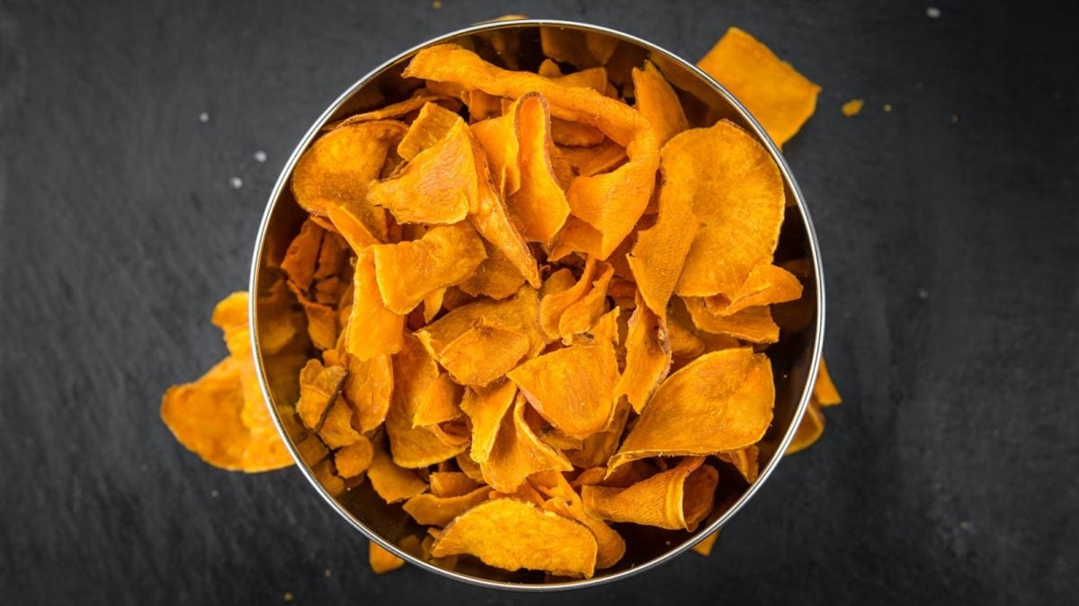 Eine Schüssel gefüllt mit gebackenen Süßkartoffel-CHips vor einem dunklen Hintergrund, von oben.