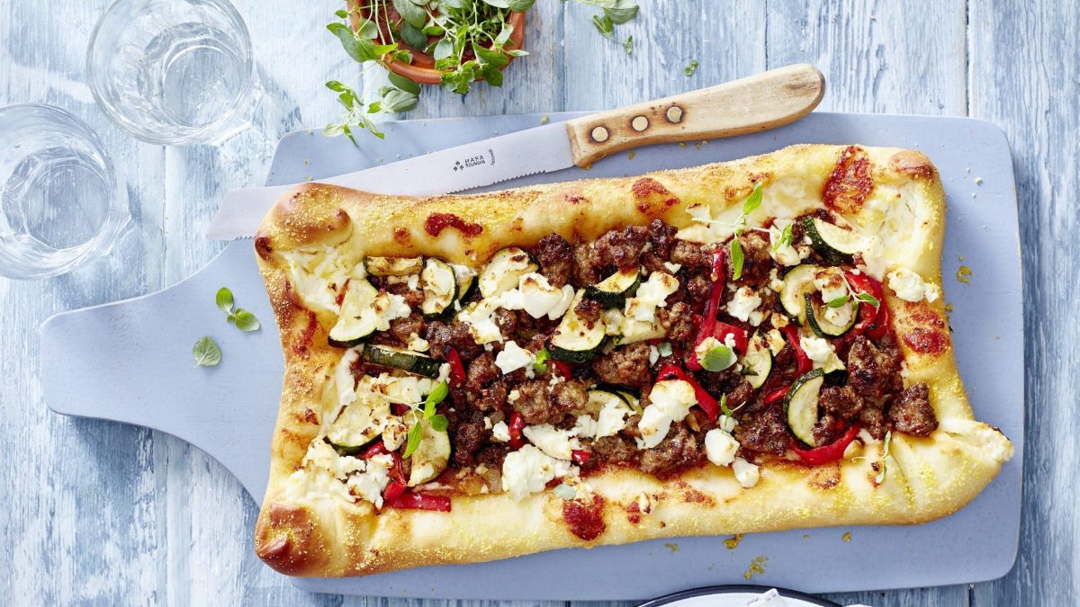 Die gebackene Gyros-Hack-Pizza liegt essbereit auf einem Brett.