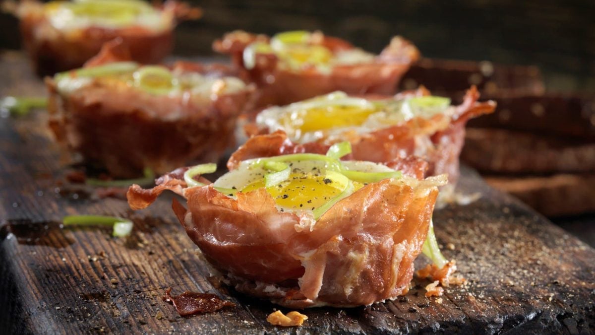 Herzhafte Muffins mit Prosciutto und Ei auf einem dunklen Holzbrett.