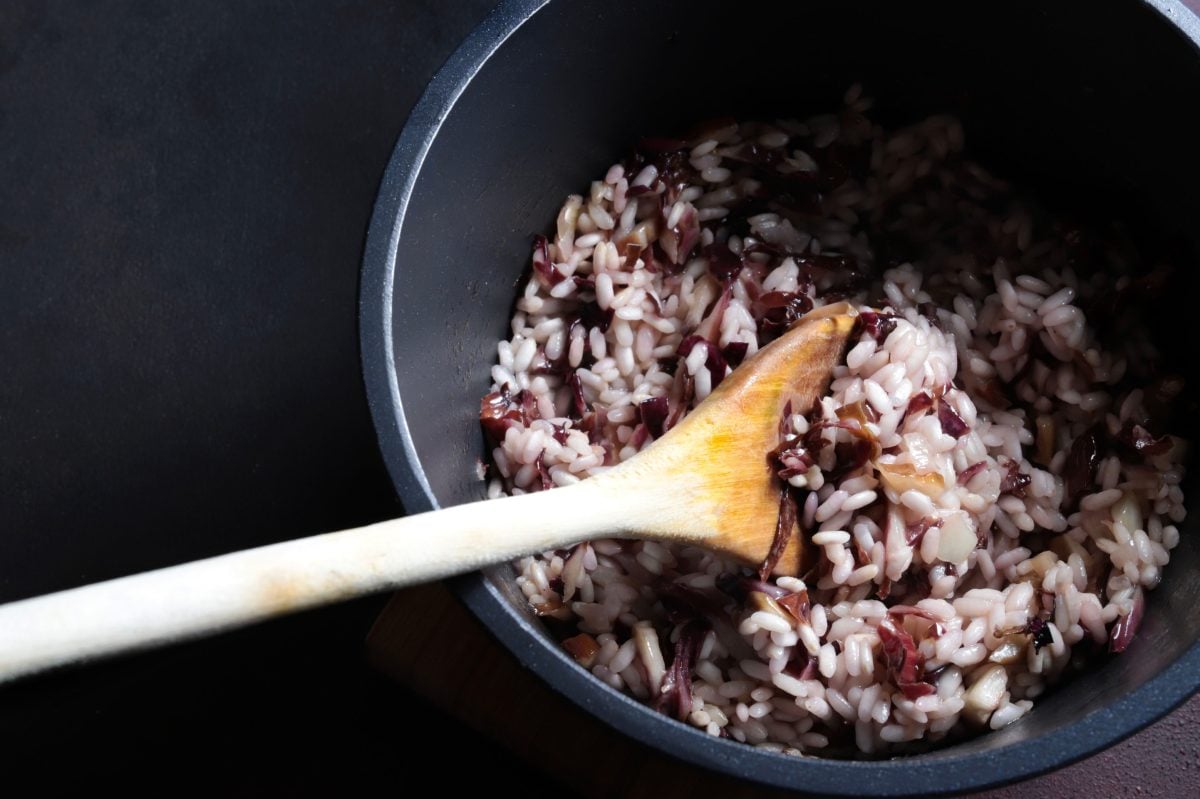 in einem dunklen Topf ist ein italienisches Radicchio-Risotto. In diesem steckt ein großer Kochlöffel au Holz.
