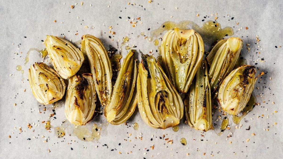 Ein Stück Backpapier, auf dem Stücke von karamellisiertem Fenchel liegen, bestreut mit Pfeffer und Öl.