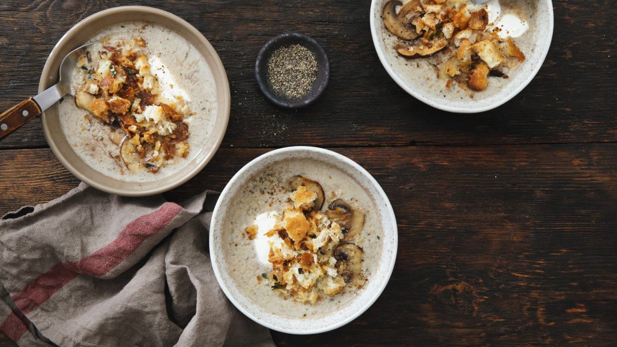 Drei Schüsseln Kartoffelsuppe mit Steinpilzen und Croutons auf dunklem Holz in der Draufsicht.