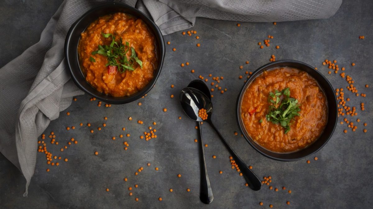 Zwei Schüsseln Rote Linsensuppe auf einem Tisch, dazu zwei Löffel und ein graues Geschirrtuch.