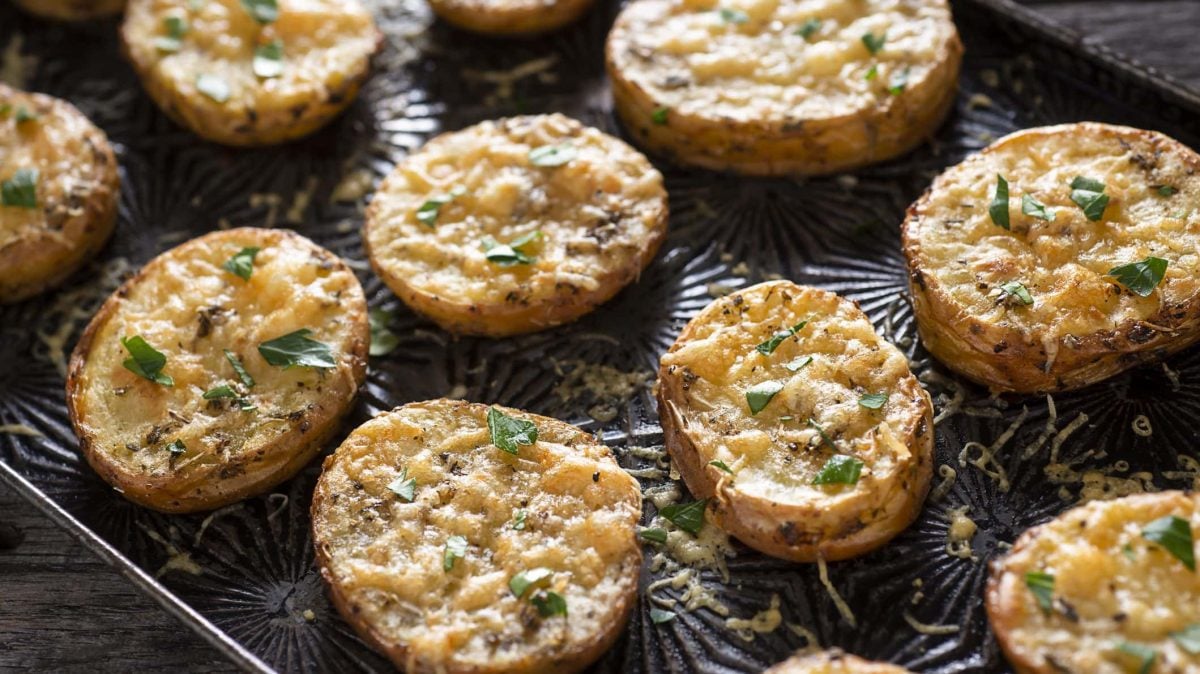 Ein Backblech mit Parmesan-Kartoffeln, die mit Kräutern bestreut sind.