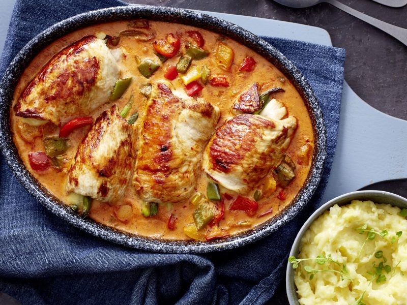 In einem großen Bräter sind Putenrouladen in Paprika-Sahne-Sauce. Daneben steht eine Schale mit Kartoffelpüree.