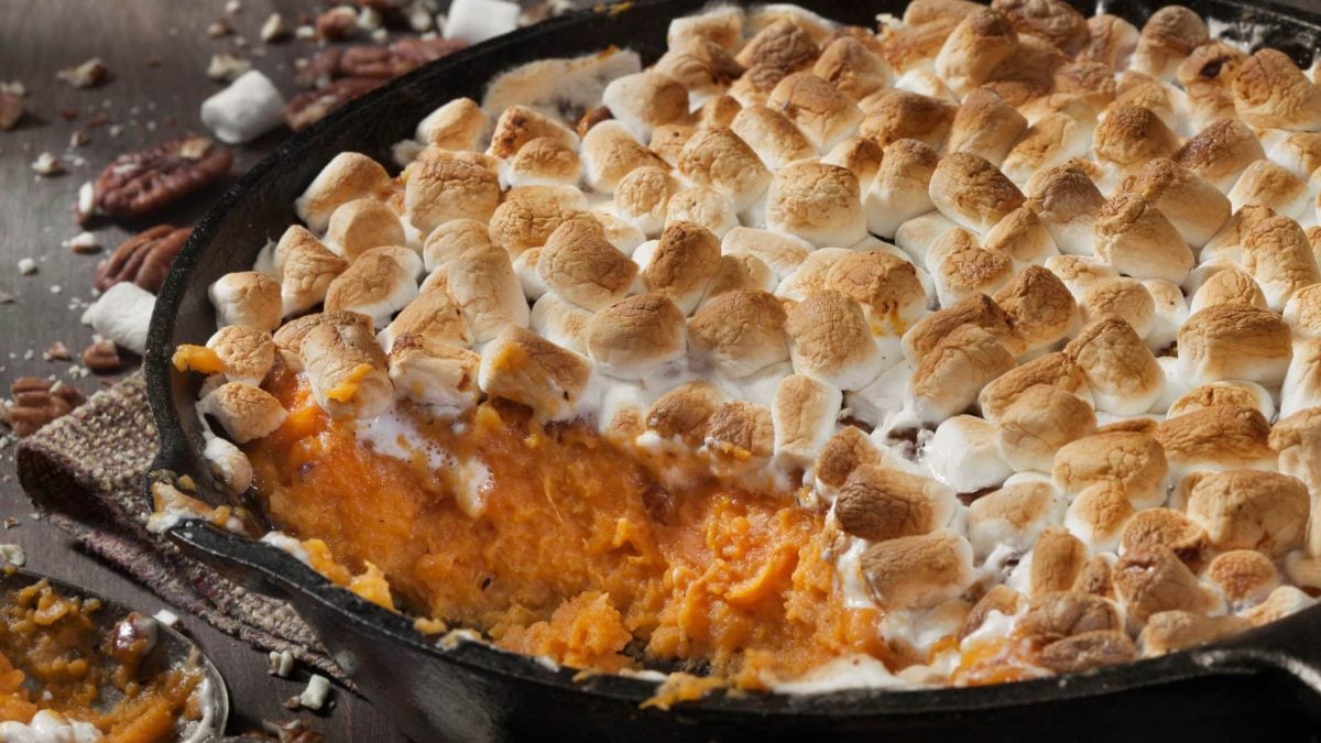 EIne dunkle Auflaufform mit Süßkartoffelauflauf mit Marshmallows. Drumherum liegen ein paar Pecannüsse.