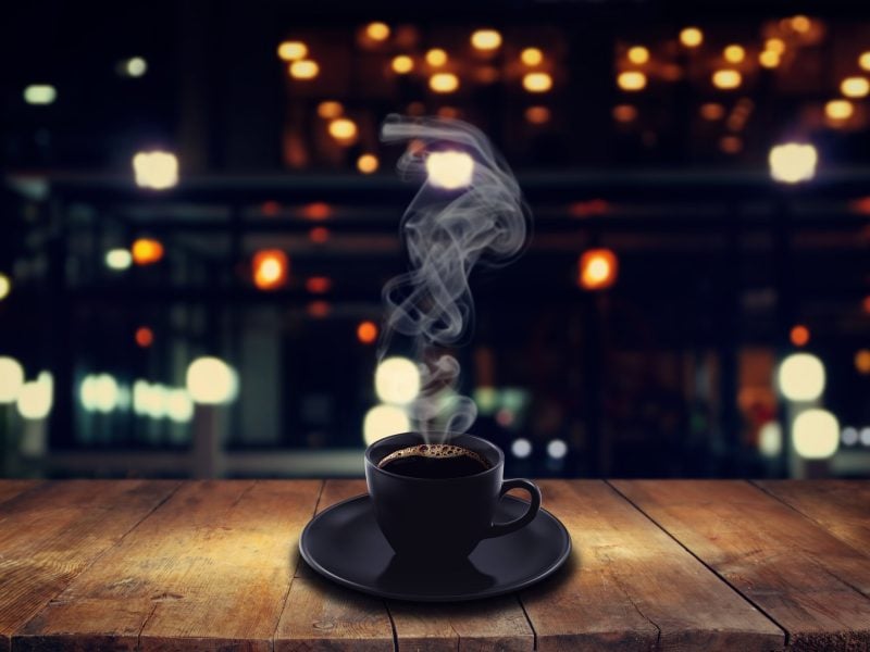 Tasse dampfender Kaffee steht auf dem Tresen einer dunklen Bar