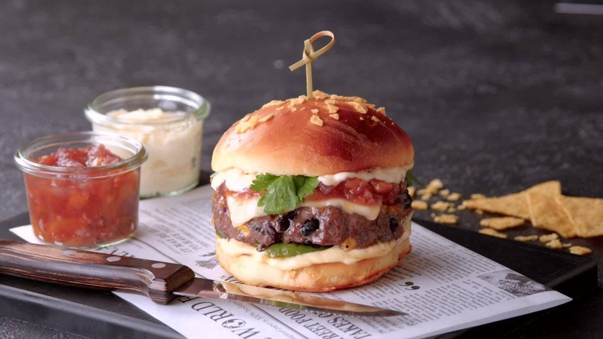 Burger mit Chili-con-Carne-Patty und Käse überbachen. Angerichtet auf einer dekorativen Zeitung auf Schieferuntergrund.