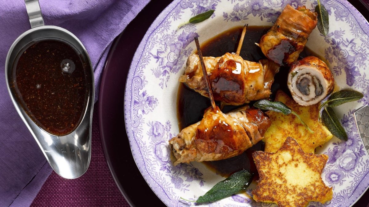 Die Balsamico-Rouladen mit Polenta-Sternen liegen mit etwas Salbei angerichtet auf einem tiefen Teller. Dazu gibt's Balsamico-Soße aus einer Sauciere.