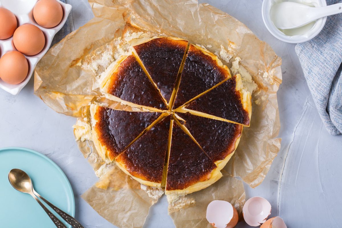 verbrennter Käsekuchen auf hellem Untergrund umgeben von Zutaten.