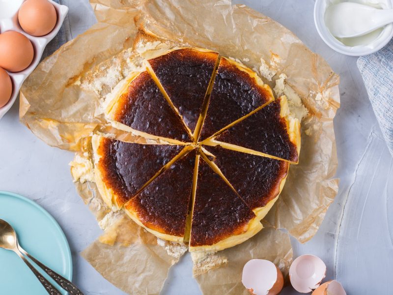 verbrennter Käsekuchen auf hellem Untergrund umgeben von Zutaten.