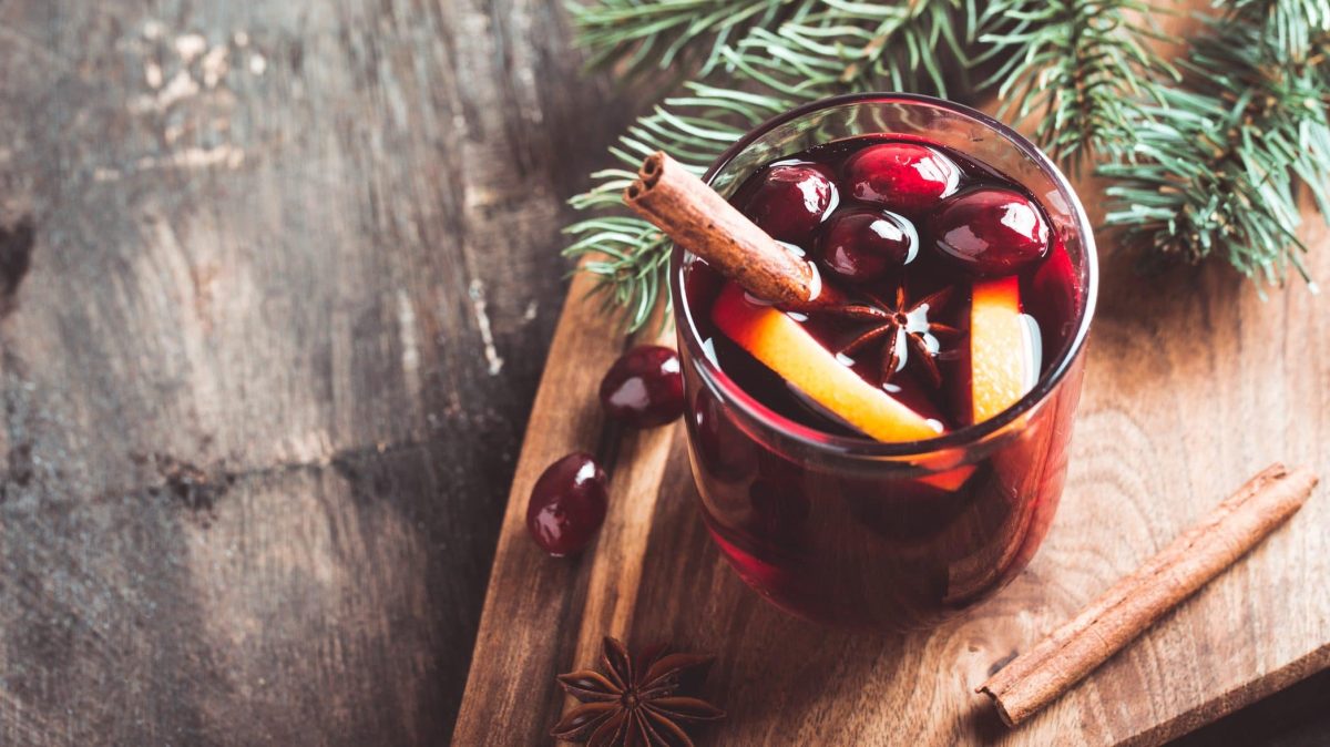 Unser Glühwein ohne Alkohol im Glas steht auf einem Holzbrett. Als Deko Gewürze und Tannenzweige.