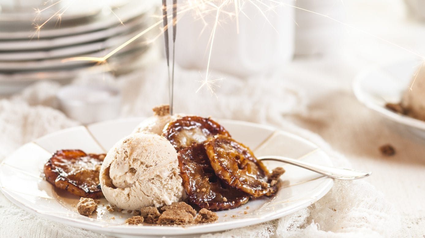 Unser Spekulatius-Eis weihnachtlich mit Wunderkerze auf weißen Tellern und Geschirr im Hintergrund in Szene gesetzt.