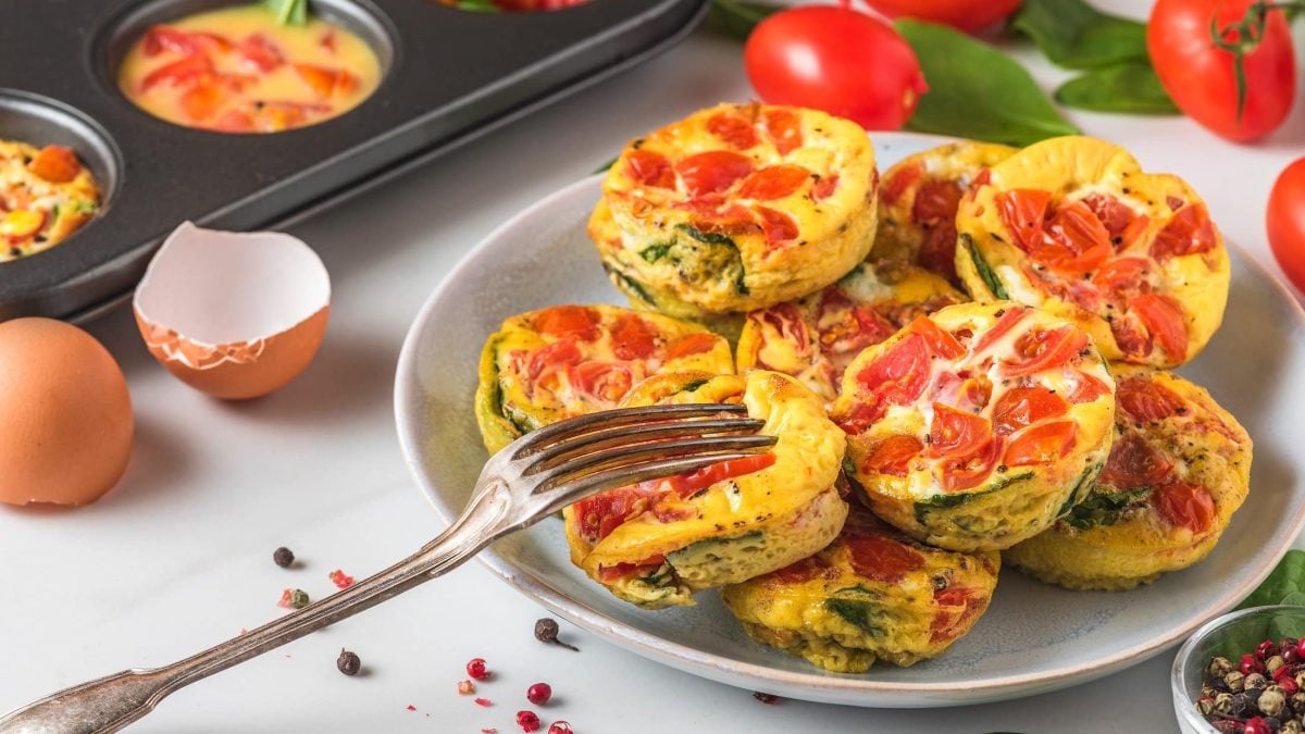 Teller mit herzhaften Muffins mit Spinat und Tomate neben Muffinblech.