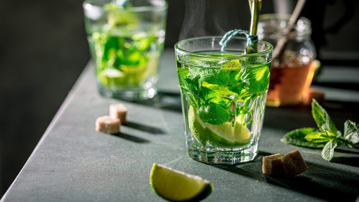 Heißer Hugo mit Limette und Minze umgeben von verschiedenen Zutaten.