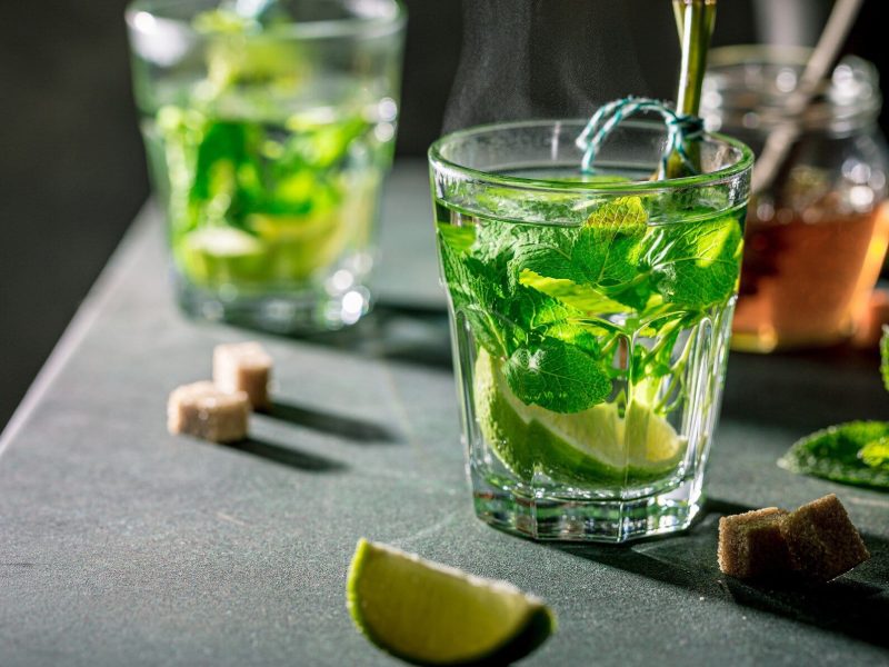 Heißer Hugo mit Limette und Minze umgeben von verschiedenen Zutaten.