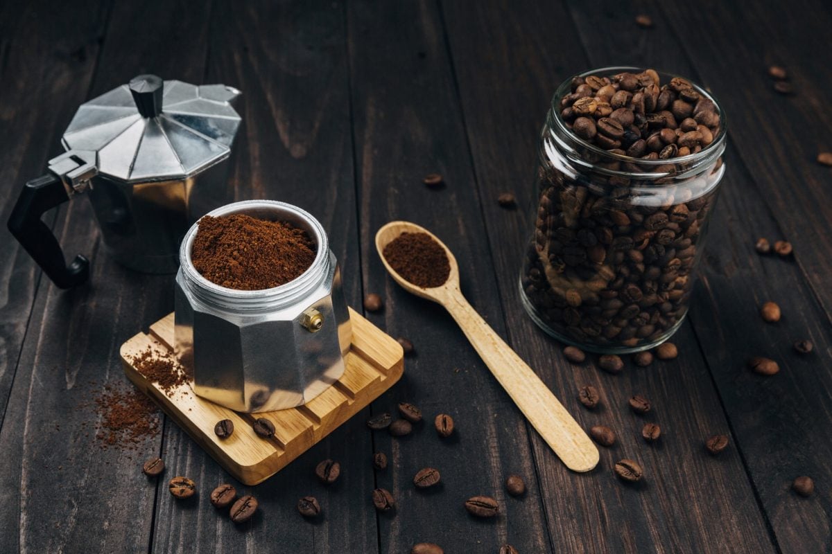 Kaffeebohnen, gemahlener Kaffee und ein Espressokocher auf dunklem Holz