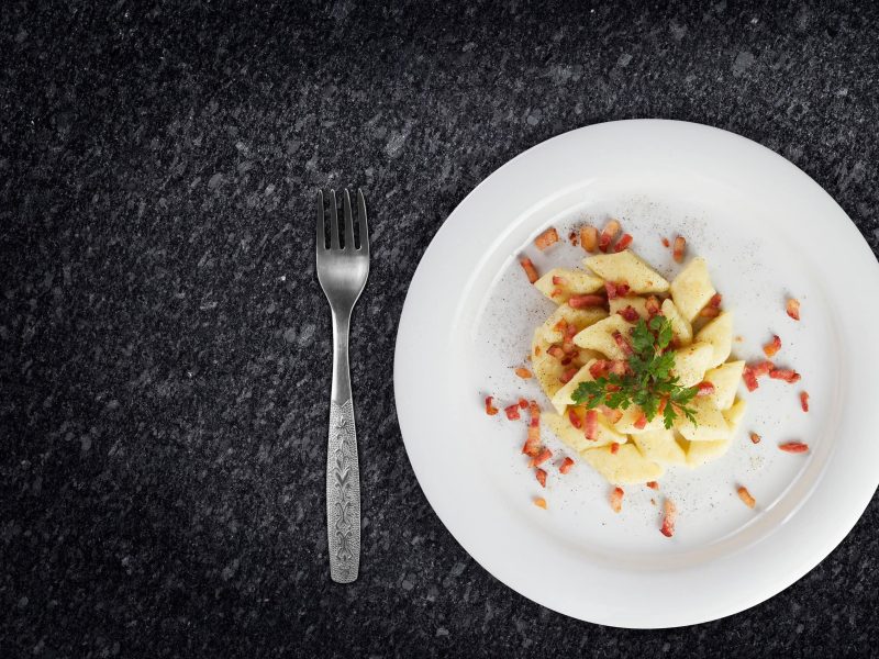 Polnische Kartoffelklöße Kopytka auf weißem Teller, serviert auf dunkler Arbeitsplatte.