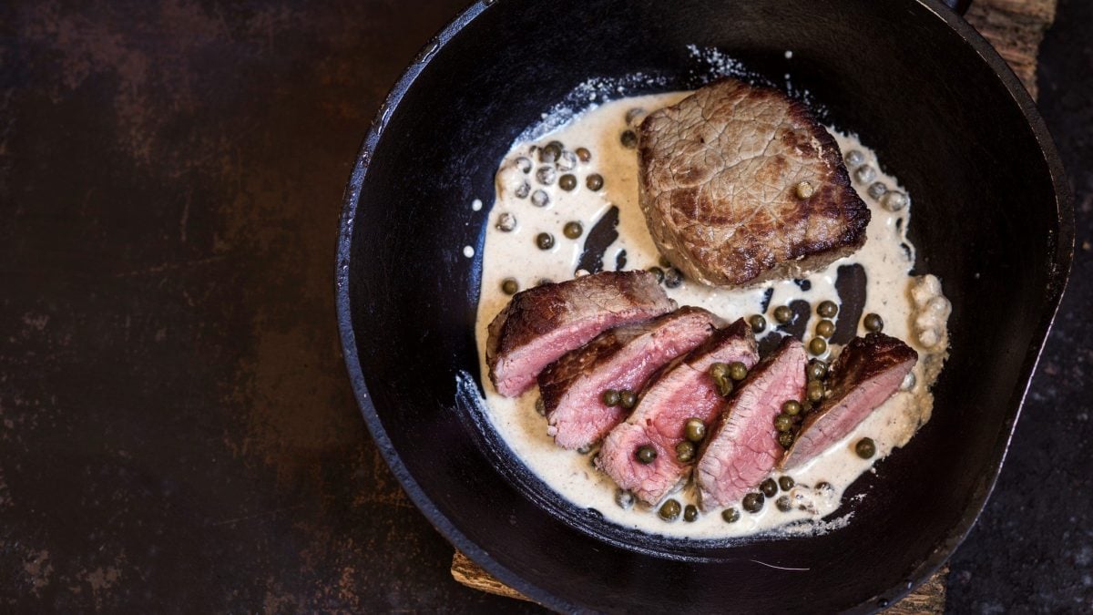 Pfanne mit Steak in Pfefferrahmsauce auf dunklem Untergrund