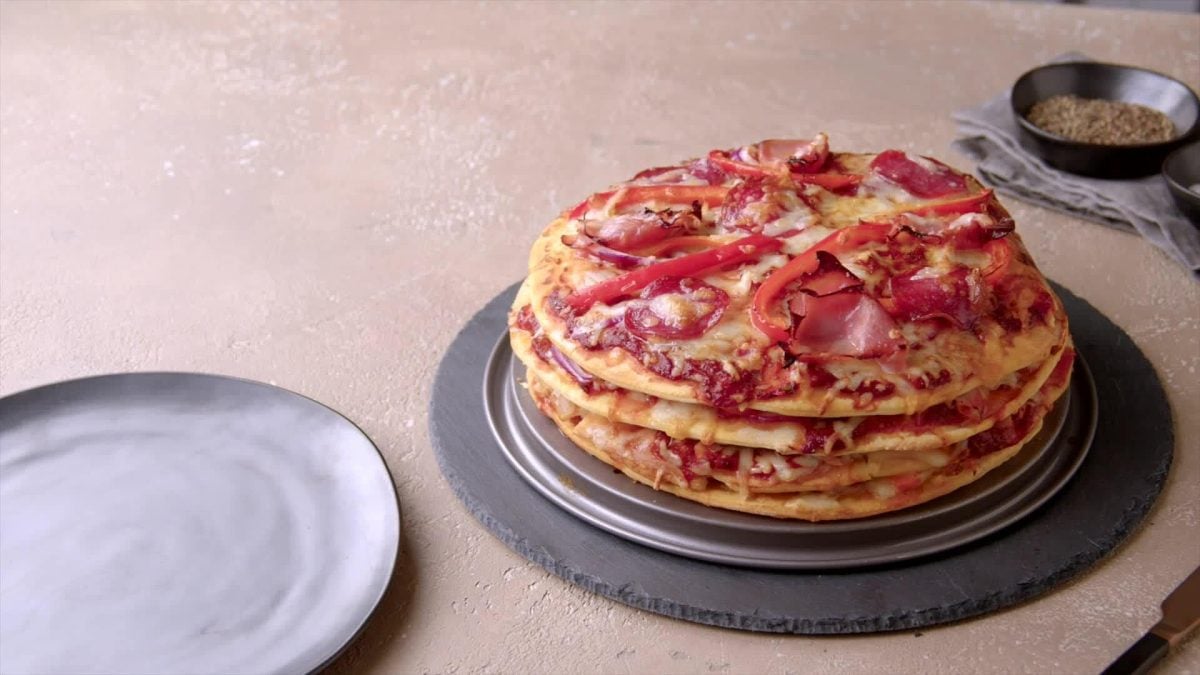 Pizzakuchen belegt mit Wurst und Paprika auf Schieferplatte.