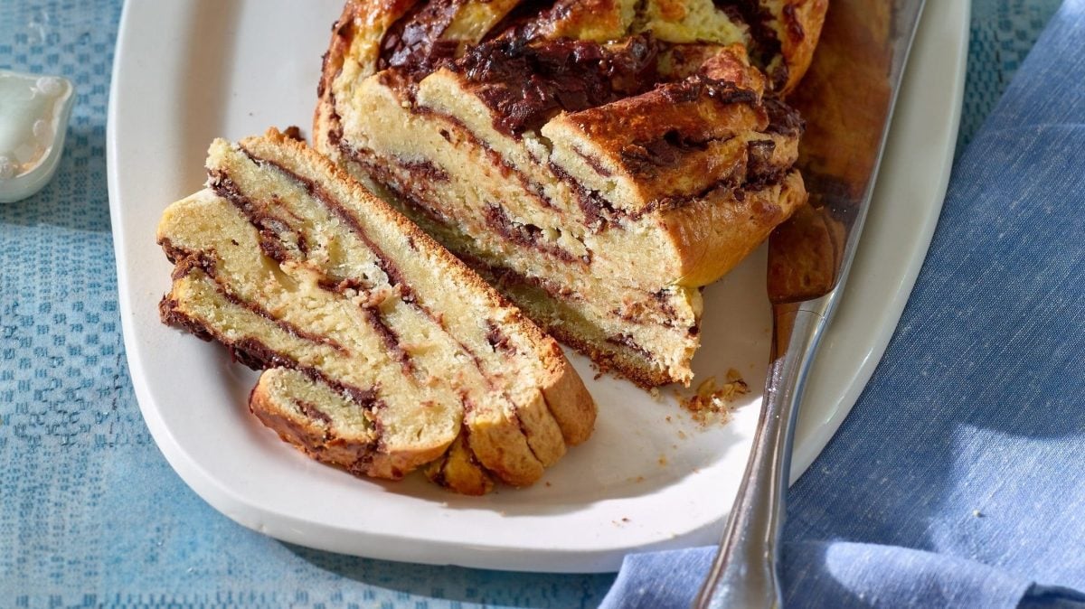 Der Schokoladen-Stollen liegt auf einer weißen Kuchenplatte. Ein Stück ist bereits abgeschnitten.