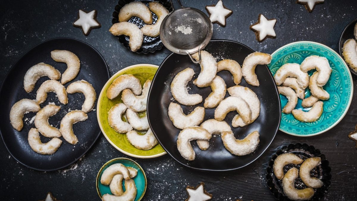 Vanillekipferl auf mehreren Tellern auf dunklem Untergrund