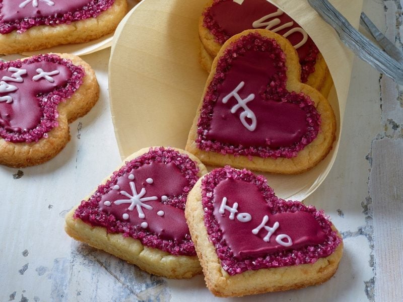 Weihnachtsherzen, Plätzchen in Herzform, mit roter Lebensmittelfarbe bemalt und mit weißer Farbe beschriftet.