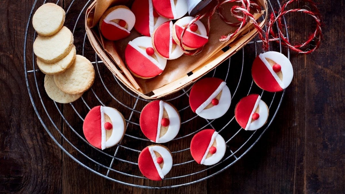 Mehrere Weihnachtsmann-Kekse liegen verteilt auf einem Gitter und in einem kleinen Korb auf einem dunelbraunen Tisch.