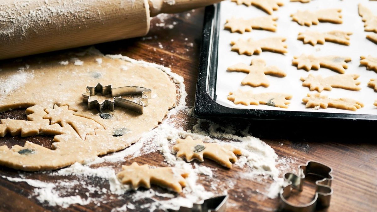 Ausgestochene Plätzchen mit weihnachtlichen Motiven auf hölzernem Untergrund.