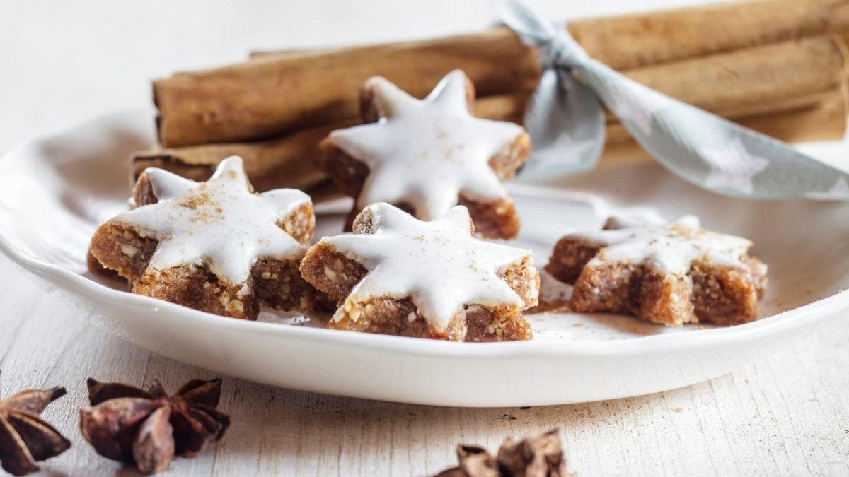 Zimtsterne mit Glasur auf weißem Teller umgeben von weihnachtlicher Dekoration.